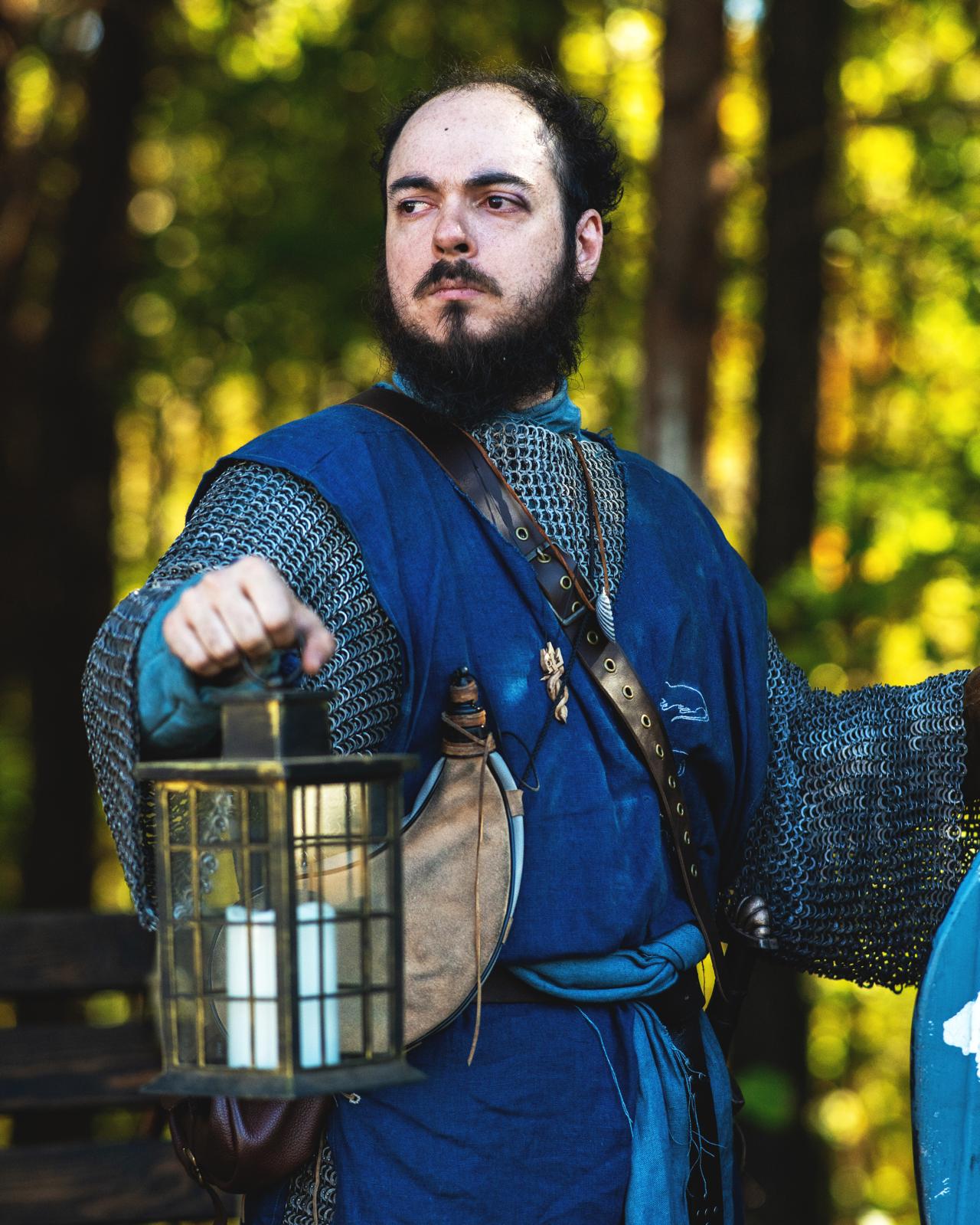 Harald, a fantasy Norman-esque warrior in blue, holding a lantern and gazing into the distance